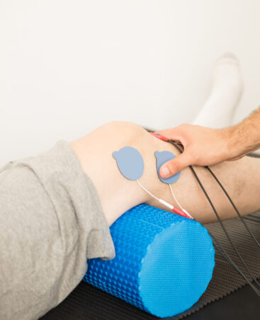 Closeup of physiotherapist's hand positioning electrodes on patient's knee in hospital